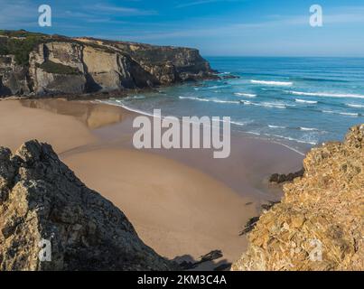 Vue sur la plage vide de Praia do Carvalhal avec vagues de l'océan, falaises et pierres, sable doré humide et végétation verte sur la côte sauvage de Rota Vicentina, Odemira Banque D'Images