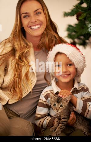 Portrait de famille à Noël, enfant avec chat et mère en vacances festives ensemble dans la maison de Dallas. Bonne maman qui donne le chaton comme cadeau à l'enfant Banque D'Images