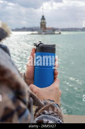 Gros plan de la main mâle tenant la coupe thermos avec la tour de jeune fille en arrière-plan. L'hiver à Istanbul. Banque D'Images