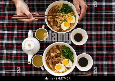 Morceau de poulet en baguettes avec des mains de ramen japonais et de mâles Banque D'Images