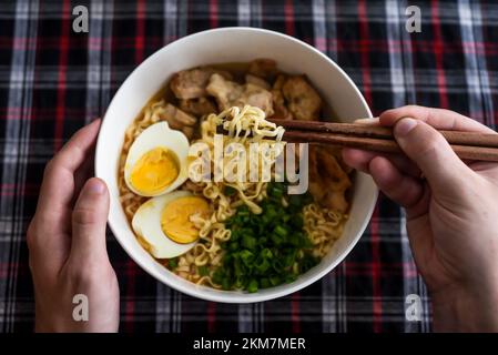 Morceau de nouilles dans des baguettes avec des mains de ramen japonais et de mâles Banque D'Images