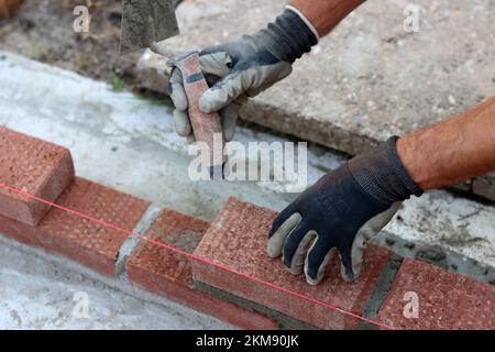 Construire un mur de briques rouges. Mains mâles tenant la truelle de brique et l'outil de mesure de niveau. Travaux de maçonnerie en détails. Photo de près du chantier de construction. Banque D'Images