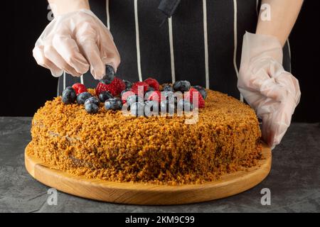 Un chef féminin décorera un gâteau de carottes maison avec des baies fraîches sur un fond sombre. mise au point sélective Banque D'Images