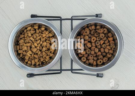 Nourriture sèche pour chats et chiens dans des bols en métal sur fond de bois blanc. Vue de dessus. Banque D'Images