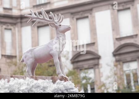 Décor blanc cerf sur le dessus d'un stand à une foire de Noël pendant la saison de vacances regardant majestueux avec des bâtiments en arrière-plan Banque D'Images