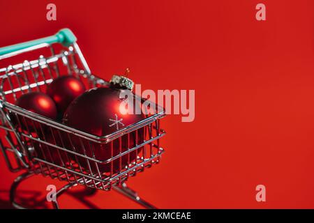 Chariot de Noël avec décorations de Noël rouges boules sur fond rouge. Minimum Noël shopping vente Web bannière copier espace concept. Banque D'Images