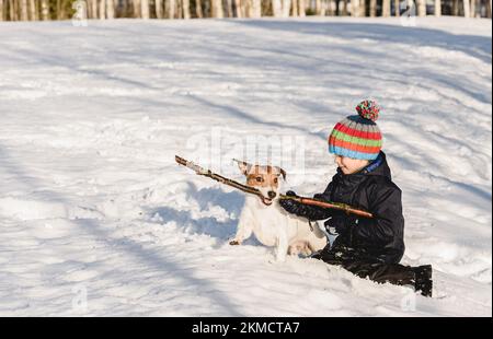 L'hiver s'amuser en plein air. Garçon jouant avec un chien de compagnie de famille sur la neige le jour d'hiver ensoleillé Banque D'Images