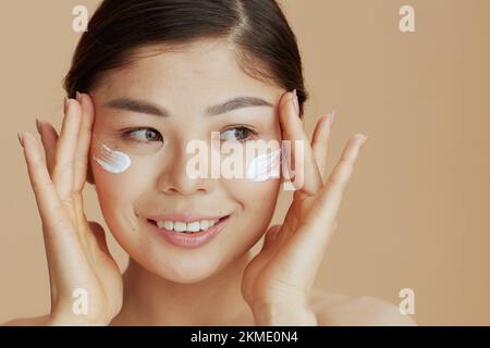 Portrait d'une femme asiatique moderne avec crème faciale sur fond beige. Banque D'Images