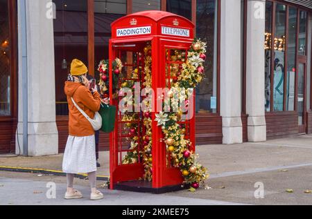 Londres, Angleterre, Royaume-Uni. 26th novembre 2022. Une femme prend une photo d'une boîte téléphonique rouge décorée d'ornements de Noël à Paddington. (Image de crédit : © Vuk Valcic/ZUMA Press Wire) Banque D'Images