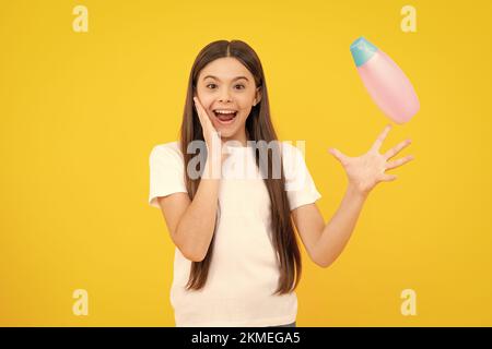 Portrait heureux de l'enfant avec après-shampooing. Soins cosmétiques quotidiens. L'adolescent de 12, 13, 14 ans tient une bouteille de soins pour les cheveux et la peau. Beauté Banque D'Images
