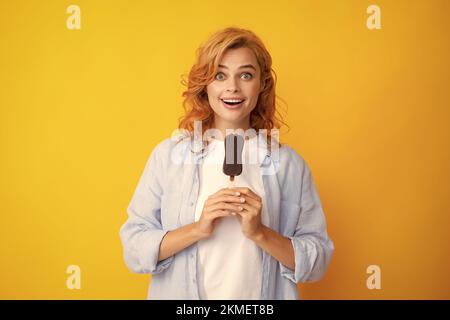 La jeune femme mange des crèmes glacées au chocolat sur fond jaune. Drôle femme de tête rouge avec de la crème glacée. Stupéfait surprise visage de femme. Banque D'Images