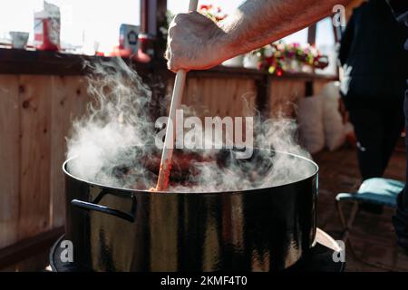 Main mâle remuant ajvar dans un grand pot. Ajvar, préparation traditionnelle de repas Banque D'Images