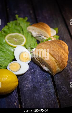 croissant frais avec thon, laitue et œuf sur fond de bois. Banque D'Images