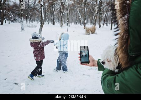 Jeux amusants les enfants peuvent jouer dans la neige. Activités d'hiver en plein air pour les enfants et la famille. Mère photographiant les enfants. Les garçons s'amusent, jouent Banque D'Images