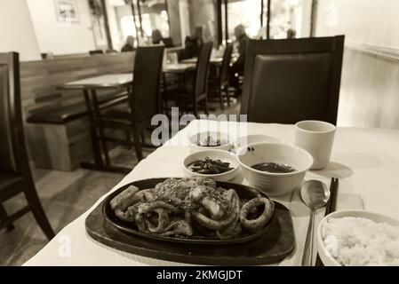 Le calamar frit et la soupe, le riz et les légumes en accompagnement dans un restaurant coréen authentique servant des plats frais simples traditionnels. Paris, France. Sépia Banque D'Images