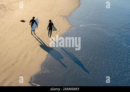 Deux surfeurs marchent le long du rivage sur Oceanside City Beach à Oceanside, en Californie. Banque D'Images