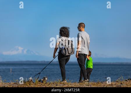 Une jeune famille heureuse qui passe du temps ensemble à l'extérieur dans la nature, au bord de la mer. Famille active avec chien marchant dans le parc. Photo de voyage, espace de copie pour texte-O. Banque D'Images