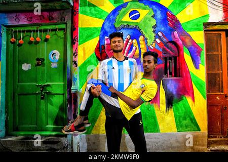 Kolkata, Inde. 26th novembre 2022. Un jeune portant un maillot de l'Argentine porte son ami en maillot du Brésil tout en posant devant un mur graffiti célébrant le tournoi de football de la coupe du monde de la FIFA 2022, à Kolkata. Crédit : SOPA Images Limited/Alamy Live News Banque D'Images