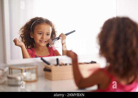 Apprendre les tenants et les aboutissants de la beauté dès le plus jeune âge. une petite fille appliquant un fard à joues dans le miroir. Banque D'Images