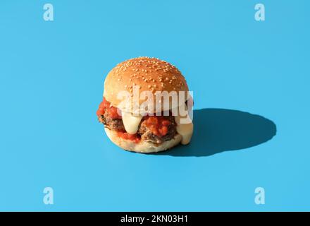 Hamburger maison avec boulettes de viande, sauce tomate et sauce cheddar blanche. Délicieux hamburger dans une lumière vive minimaliste sur une table bleue. Banque D'Images