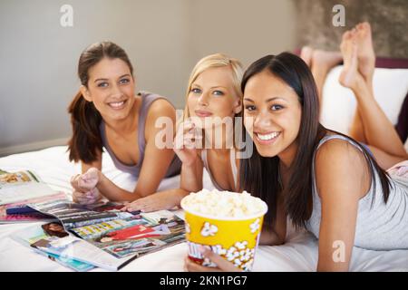 Les soirées pour dames sont les meilleures. trois jeunes femmes attirantes qui traînaient dans une chambre à coucher pour manger du pop-corn et lire des magazines. Banque D'Images