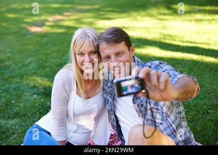 Allons en prendre un pour les enfants. un couple séduisant prenant un selfie dans le parc. Banque D'Images