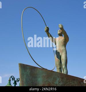 Lixouri, promenade du port, sculpture en bronze, frontale d'en-dessous, homme avec grand pneu, ciel bleu sans nuages, île de Kefalonia, Iles Ioniennes, Grèce, EUR Banque D'Images