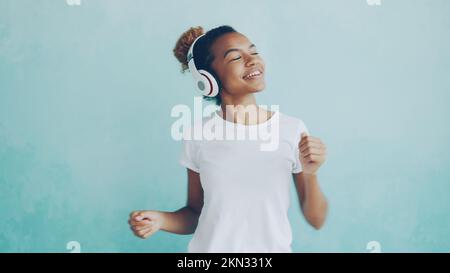 Portrait d'une femme afro-américaine heureuse écoutant de la musique à l'aide d'un casque sans fil et dansant en écoutant de la mélodie. Technologie moderne, jeunes et concept amusant. Banque D'Images