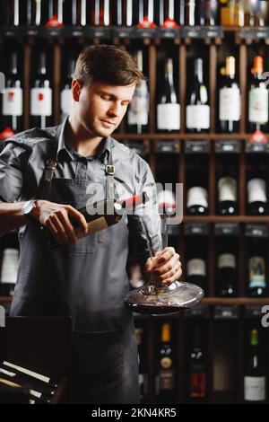 Le barman verse du vin rouge dans un récipient transparent en cave Banque D'Images