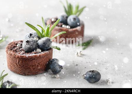 Brownies au chocolat décorées de bleuets et de romarin sur fond blanc texturé avec des lumières de bokeh. Noël, concept de recette du nouvel an. Fermer Banque D'Images