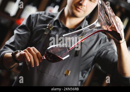 Le barman verse du vin rouge en verre dans un grand récipient transparent Banque D'Images