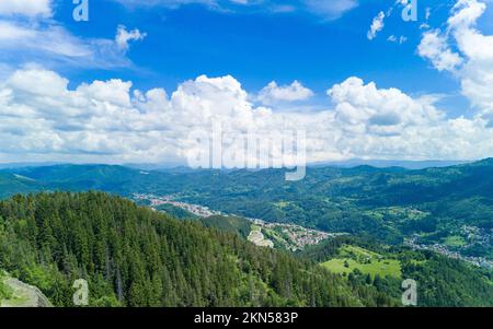 Petite ville bulgare Smolyan avec maisons et lac est couverte de végétation et de rayons de soleil sous les nuages. Montagnes Rhodope Banque D'Images