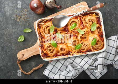 Lasagnes. Pâtes de lasagne faites maison rotolo cuire avec sauce tomate, fromage à la crème et basilic sur une poêle blanche sur fond d'ardoise sombre, de pierre ou de béton. Il Banque D'Images