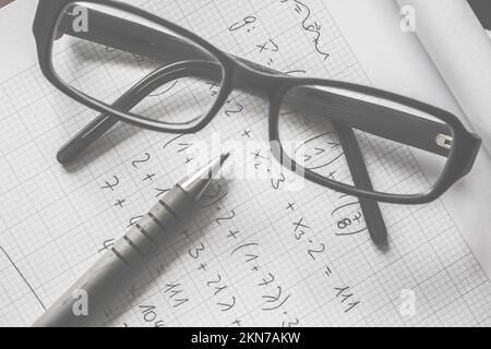 Photo d'objet noir et blanc de formules mathématiques complexes écrites sur papier graphique doublé avec stylo et lunettes optiques. L'éducation est intelligente Banque D'Images