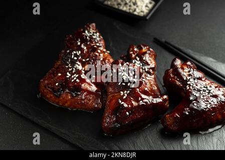 Ailes de poulet de style asiatique en sauce aigre-douce sur une assiette sur fond de pierre sombre avec espace à copier. Vue de dessus, plan plat Banque D'Images