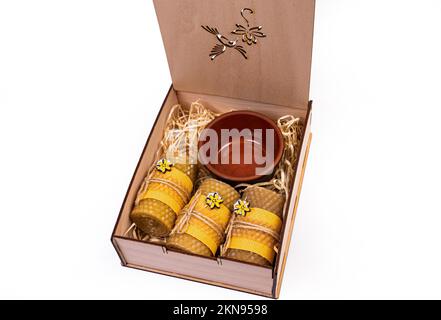 Vitamines et produits biologiques dans le cadeau. Miel dans un pot avec un bâton et des bougies de cire. Cadeau dans une boîte isolée sur blanc Banque D'Images