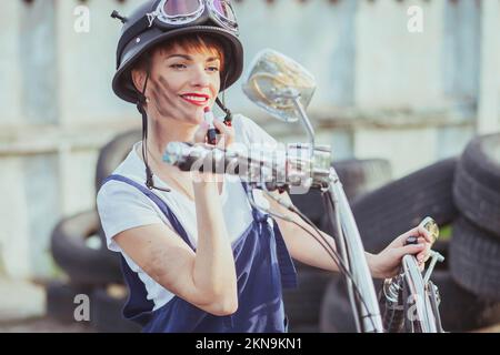 Fille auto mécanicien dans le casque regarde dans le miroir de moto et les lèvres de peinture Banque D'Images