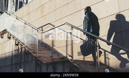 Un homme noir chauve avec une barbe monte les escaliers pour travailler. Le grand succès africain est en montant un escalier un jour ensoleillé, portant un carnet Banque D'Images