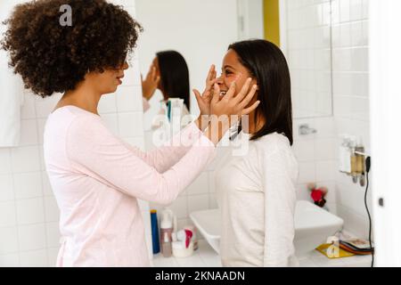Femme noire appliquant des cellules oculaires sur le visage de sa fille dans la salle de bains à la maison Banque D'Images