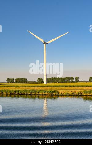 Grande éolienne dans un champ de ferme isolé contre un ciel bleu profond avec réflexion dans l'eau d'un canal. Personne. Banque D'Images