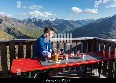Un randonneur se trouve sur la terrasse de la hutte de Brunnenkogelhaus et regarde son téléphone portable devant les Alpes de l'Ötztal et la vallée de Gurgl, en Autriche Banque D'Images