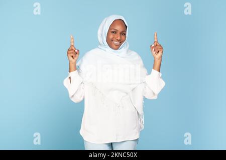 Une femme musulmane afro-américaine excitée pointant au-dessus de sa tête avec deux mains, démontrant la place libre pour votre annonce Banque D'Images