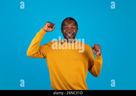 Homme afro-américain mature et positif célébrant le succès sur le bleu Banque D'Images