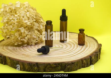 Maquette de flacons en verre brun avec couvercle compte-gouttes sur panneau en bois. Flacons en verre vides avec pipette, fleur d'hortensia séchée sur fond jaune. Concept o Banque D'Images