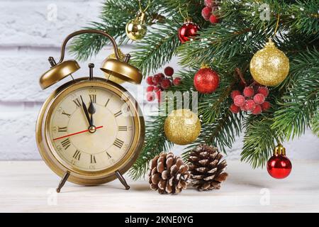 Arbre de Noël et compte à rebours pour la nouvelle année. Horloge rétro en bronze, cône et boules et branches d'épinette de sapin sur fond de brique blanche. Banque D'Images