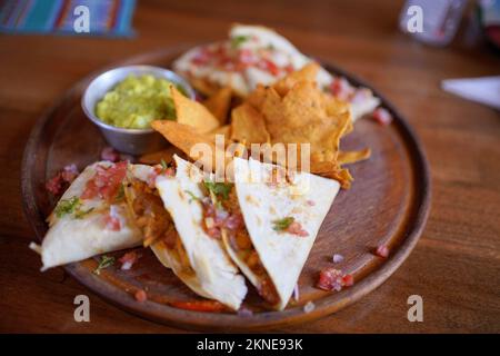 Poulet quesadilla avec nachos et guacamole sur une assiette en bois. Banque D'Images