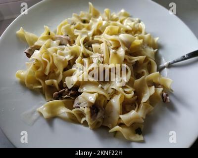 Une portion de pâtes italiennes à tagliatelle en sauce crémeuse avec jambon et champignons sur une assiette blanche Banque D'Images
