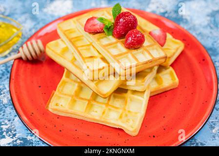 Dessert sucré de gaufres belges avec fraises et bleuets sur une assiette avec miel Banque D'Images