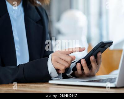 Le doigt de la femme d'affaires se touchant sur le téléphone portable. Téléphone portable intelligent noir dans la main de la personne près de l'ordinateur portable sur le bureau. Cyber-securi Banque D'Images