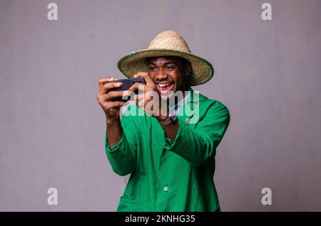 Un homme afro-américain joyeux dans une chemise verte utilisant un téléphone portable Banque D'Images